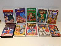 Photo displaying 11 Disney VHS movies arranged in two rows with original illustrated cases featuring classic titles.
