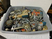 Bin filled with assorted metal hardware including window crank handles, brackets, and boxed small parts.