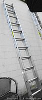 Full view of aluminum metal extension ladder leaning against wall showing rungs and side rails.
