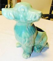 Side view of turquoise ceramic dog planter showing one head cluster and hollow body opening.