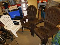 Three Adirondack style chairs placed together, one white and two brown.