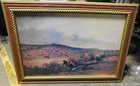 Front view of a large framed painting showing a hunt scene with riders in red jackets on horseback jumping over fences in a rural setting.
