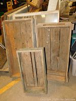 Photo showing three old wooden crates of varying sizes standing upright in an indoor setting. Crates are worn with visible wood grain and nail heads.
