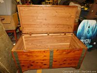 Front angled view of the large cedar storage chest with lid open, showing exterior wood and metal reinforced corners.
