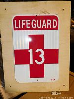 Photo of one side of the double sided lifeguard sign showing the number 13, red cross, and LIFEGUARD text.