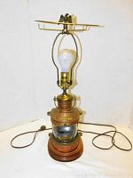 Full view of the lamp showing wooden base, clear glass section, copper/bronze metal housing, bulb, harp and power cord.