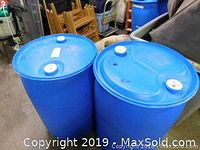 Blue plastic rain barrel with white screw-on lids, shown in interior storage or warehouse setting.
