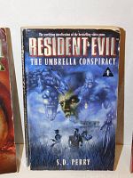 Close-up of Resident Evil: The Umbrella Conspiracy paperback book cover with horror-themed illustration