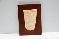Front view of the carved indigenous face mask on wooden plaque