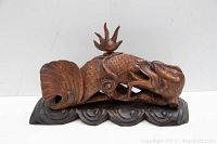 Front and side views of the carved mythical eel dragon sculpture resting on a carved wooden base with wave designs.