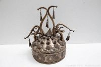 Front angle view of silver-tone Chinese matrimonial celebratory hat showing embossed floral patterns and conical top elements with dangling tassels.