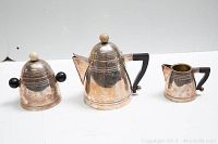 Three-piece metal tea set including teapot, creamer, and sugar bowl shown in a straight view on white surface with plain background.