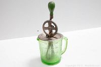 Full view of vintage egg beater mounted on green glass measuring cup with handle and visible volume markings.