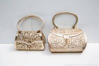 Pair of two metal evening purses with decorative embossed and cut-out detailing placed side by side.