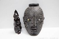 Photo showing black carved tribal style mask with white swirl patterns and black glazed ceramic figure statue side by side.