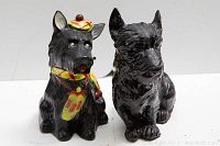 Front view of both Scottish Terrier figurines, the piggy bank with colorful scarf and cap and the solid black figurine.