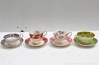 Four vintage porcelain teacups and saucers arranged in a line showing different color schemes and gilded floral designs.