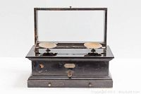 Front view of vintage apothecary scale with glass top lifted showing two round metal trays for weighing.