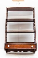 Front view of the wooden hanging shelf showing four shelves and a drawer with two white knobs.