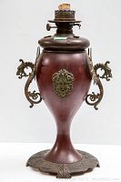 Front view of lamp showing urn-shaped body, lion mask medallion and round burner assembly