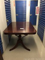 Mahogany rectangular dining table on pedestal base in storage unit with blue doors.