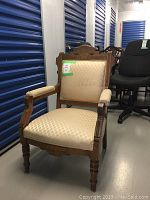 Front view of vintage wooden armchair showing carved wood frame and beige patterned upholstery.