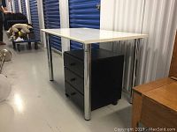 Side view of white desk with metal legs and black cabinet with drawers underneath.