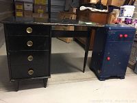 Photo showing full view of vintage black desk with four drawers and dark blue bedside table with three red knobs, both items show wear.