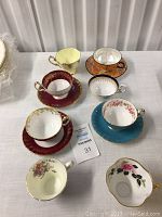 Collection of varied vintage porcelain teacups and saucers arranged on a table, showing distinct colors, floral and gold accents.