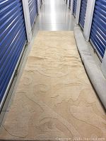 Full view of sand coloured wool carpet with textured floral swirl pattern rolled partially at one end.