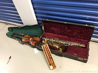 Overview of violin in green case, saxophone in red velvet case, and recorder in box
