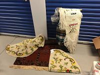 Three Persian-style rugs stacked: one small rectangular rust-colored rug with fringes, two semi-circular hood rugs with cream background and floral accents.