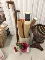 Wide view of the lot showing three wooden canes, rolled prints in a stoneware jar marked '2', pink planter with faux red roses, and wooden umbrella stand.
