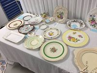 Overview of assorted Nippon, Aynsley, H & K china serving plates with varied floral designs and shapes displayed on white table.
