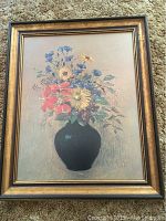 Full view of framed floral print showing bouquet in black vase on beige background with black and gold frame.