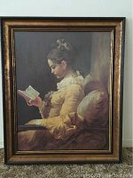 Full view of framed print showing woman reading in yellow dress, sitting on a couch with pillow, frame details visible.