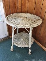 White wicker patio table full view showing two-tier design and condition of legs.