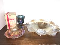 Three carnival glass pieces including a large Floragold bowl, a goblet candle in original box, and a small bowl on wooden surface