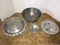Overview of the lot showing all four items on brown carpet: pie keeper with lid and handles, small basket, divided server, and pewter bowl.