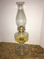 Full view of the vintage oil lamp showing clear glass chimney, amber hexagonal-patterned fuel reservoir, and pressed glass base.