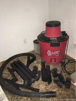 Red Sears Craftsman 16 gallon wet dry vacuum with multiple black attachments arranged around it on carpeted floor.