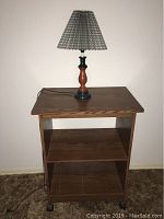Front view of the wooden Sauder style cart with the table lamp on top