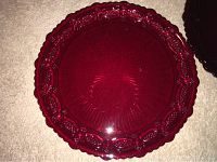 Top view of a single Avon 1876 Cape Cod Collection dinner plate in deep ruby red color showing decorative embossed border and smooth center