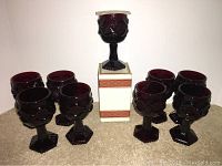 Photo showing 8 Avon Cape Cod wine goblets arranged with one goblet on top of its original box.