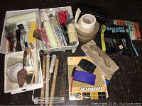 Full view of assorted painting tools, brushes, rollers, spatulas, masking tape, sanding sheets and other supplies arranged on floor.