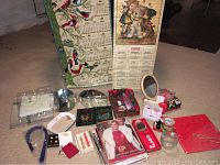 Photo showing vintage Avon catalogs, several decorative items including glass dishes, a choker necklace, a 1986 calendar with child illustrations, Santa-themed container, compact mirrors and jewelry pieces.