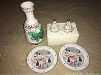 White ceramic vase with green holly and red berry decoration and a red band near the neck, standing on beige surface