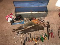 Photo showing open long metal toolbox and laid out tools including saws, hammer, wrenches, screwdrivers, grease gun, and rotary tool