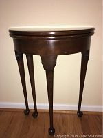 Solid wood table folded half circle against wall showing the front and legs.