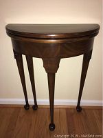 Closed view of table showing semicircular flip top folded down and supported by four legs including two gate legs.